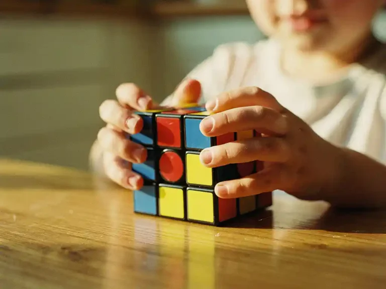 Kleine kinderhanden die een kleurrijke Rubik's kubus vasthouden aan houten keukentafel in zacht ochtendlicht