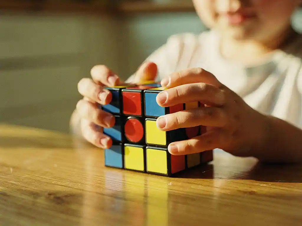 Kleine kinderhanden die een kleurrijke Rubik's kubus vasthouden aan houten keukentafel in zacht ochtendlicht