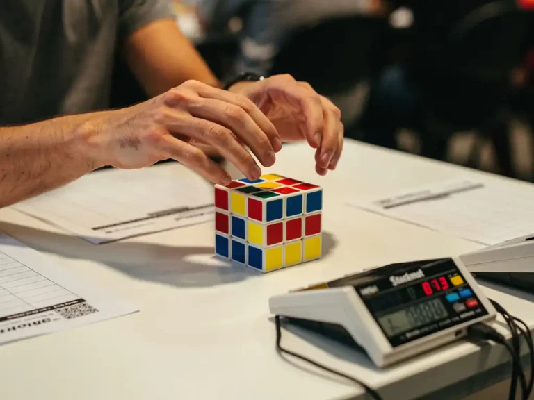 Speedcuber's handen boven kleurrijke 3x3 Rubik's kubus op competitietimer mat met WCA scramble vellen en digitale stackmat timer