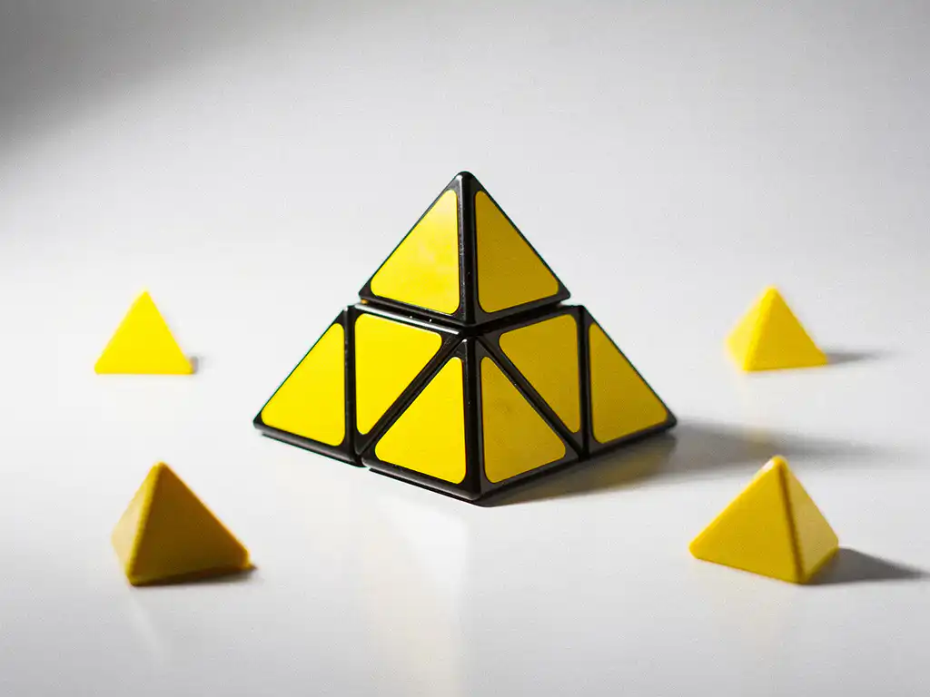 Gele pyraminx puzzel op wit oppervlak, scherpe studioverlichting benadrukt geometrische driehoekige vlakken.