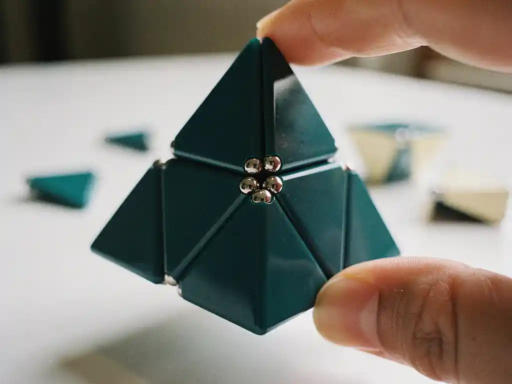 Magnetische pyraminx puzzel vastgehouden tussen twee vingers, met glanzende driehoekige vlakken en zichtbare zilveren magneetpunten.
