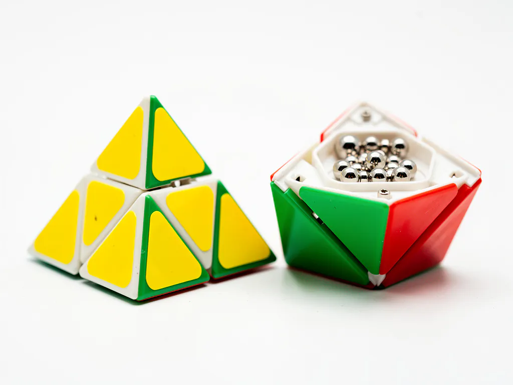 Standaard pyraminx en magnetische pyraminx naast elkaar op wit oppervlak, met zichtbare magneetcomponenten en levendige gele, groene en rode vlakken.