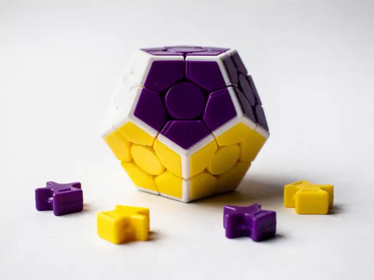 Megaminx dodecaëder puzzel met twaalf veelkleurige pentagonale vlakken op wit oppervlak, met losse stukjes rondom.