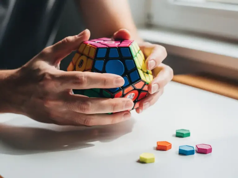 Beginnersh anden houden een kleurrijke megaminx dodecaëder puzzel vast, half opgelost op een wit bureau in natuurlijk licht.