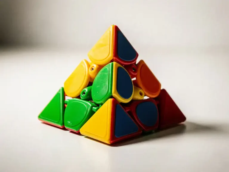 Pyraminx puzzel in geel, groen, rood en blauw met één gedeeltelijk gedraaid vlak, gefotografeerd op wit oppervlak.
